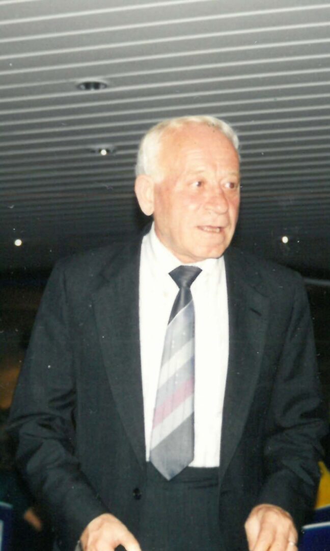 An old man wearing black suit, smiling at the camera