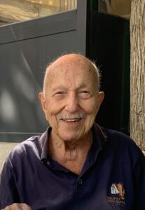 An older man with a moustache smiling at the camera.
