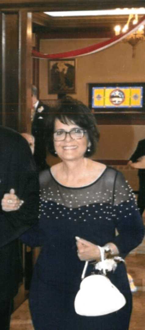 A woman in a beaded dress with glasses smiling at an indoor event.