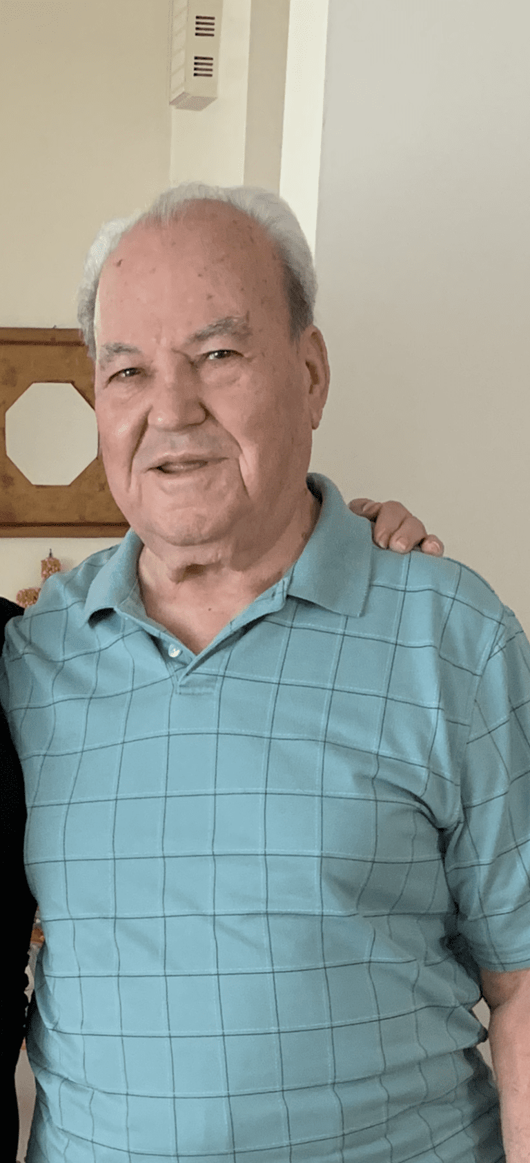 Elderly man in a blue shirt smiling indoors.