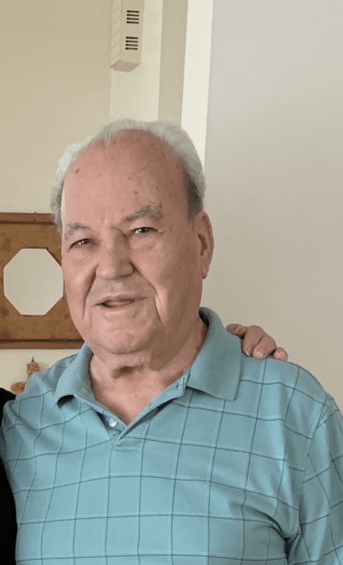 Elderly man in a blue shirt smiling indoors.
