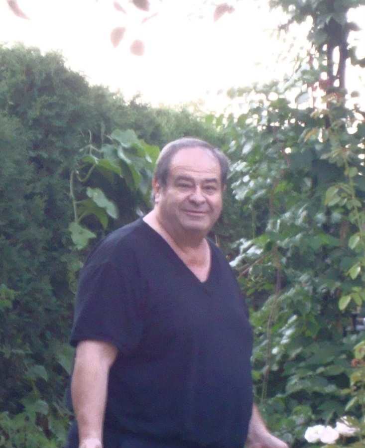 Man standing in a garden with green foliage in the background.