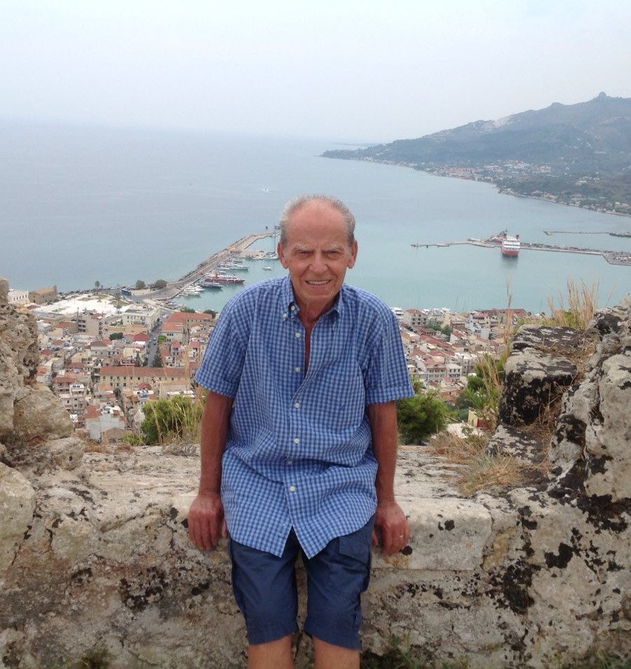 An older man sitting on top of a cliff overlooking the sea.