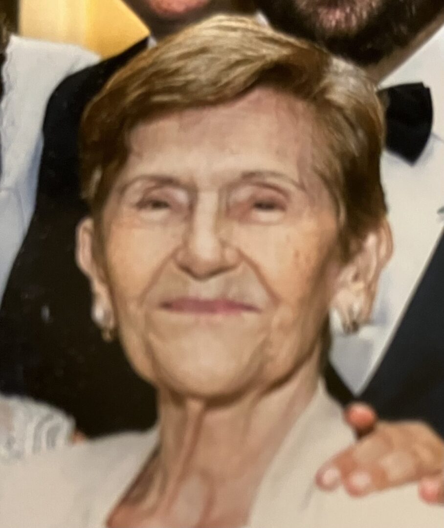 An elderly woman smiling at the camera with others nearby.