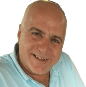 Man with a bald head smiling at the camera, wearing a light blue shirt against a green background.
