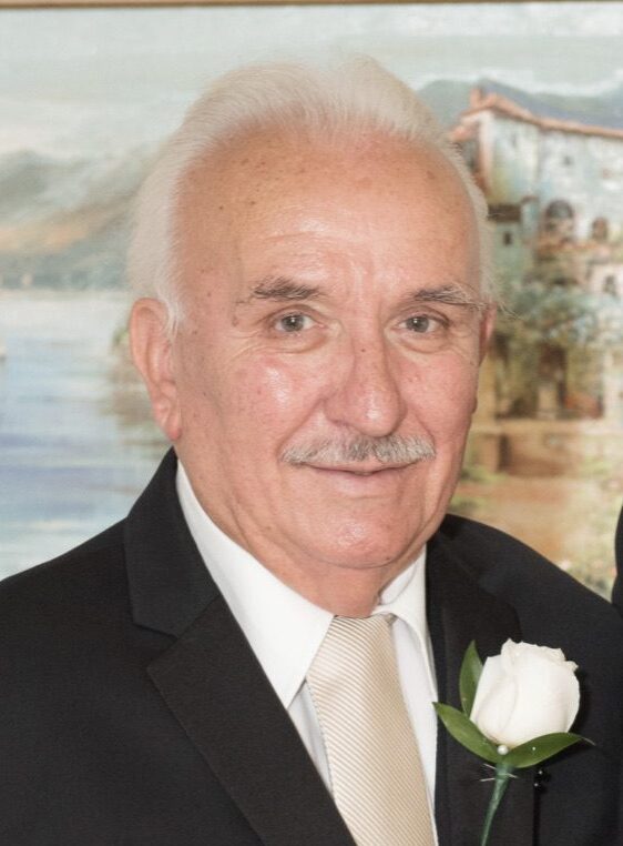 An elderly gentleman with a white boutonniere smiling at the camera.