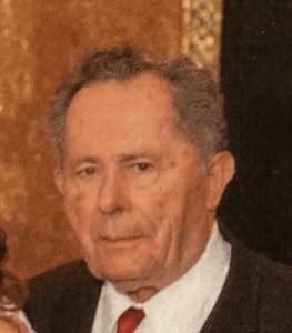 A mature man in a suit and tie with a solemn expression.