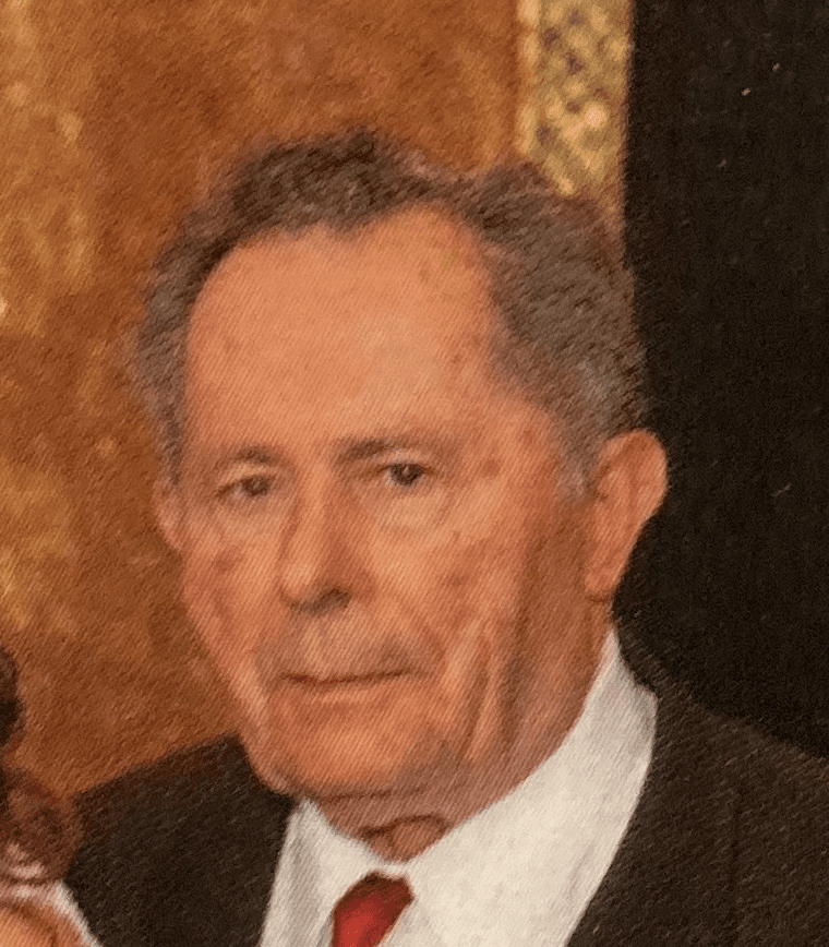 A mature man in a suit and tie with a solemn expression.