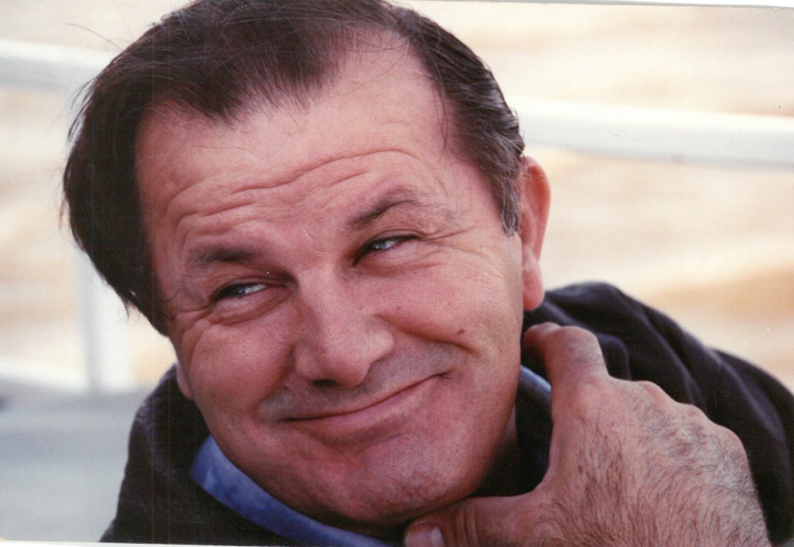 A man with a wry smile resting his chin on his hand.