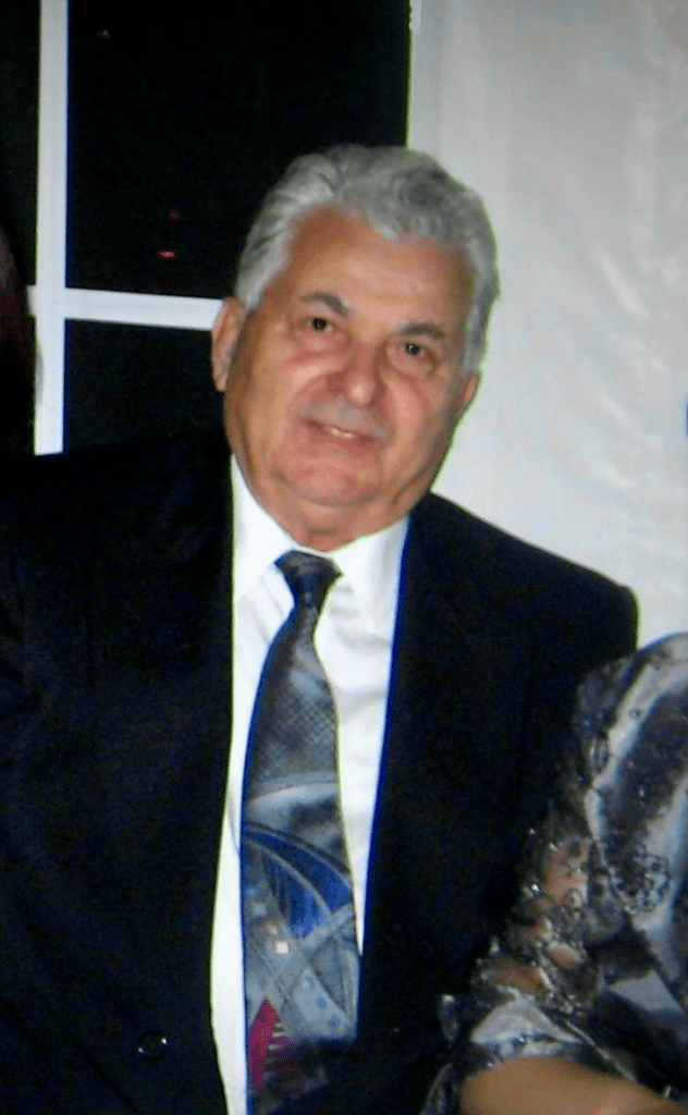An older gentleman with gray hair wearing a suit and tie smiling at the camera.
