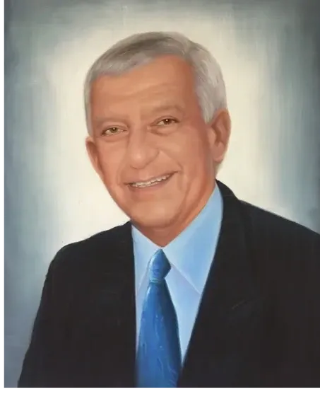 Portrait of a smiling elderly man with gray hair wearing a suit and blue tie.