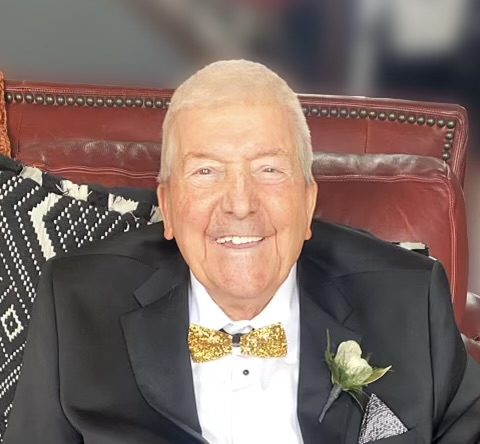Elderly gentleman smiling in a black tuxedo with a gold bow tie and boutonniere.