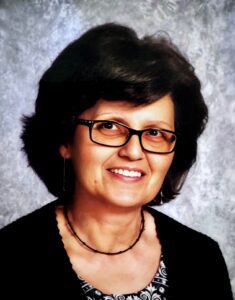 Smiling woman with glasses and necklace.