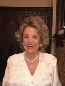Smiling woman in a white blouse with a pearl necklace.